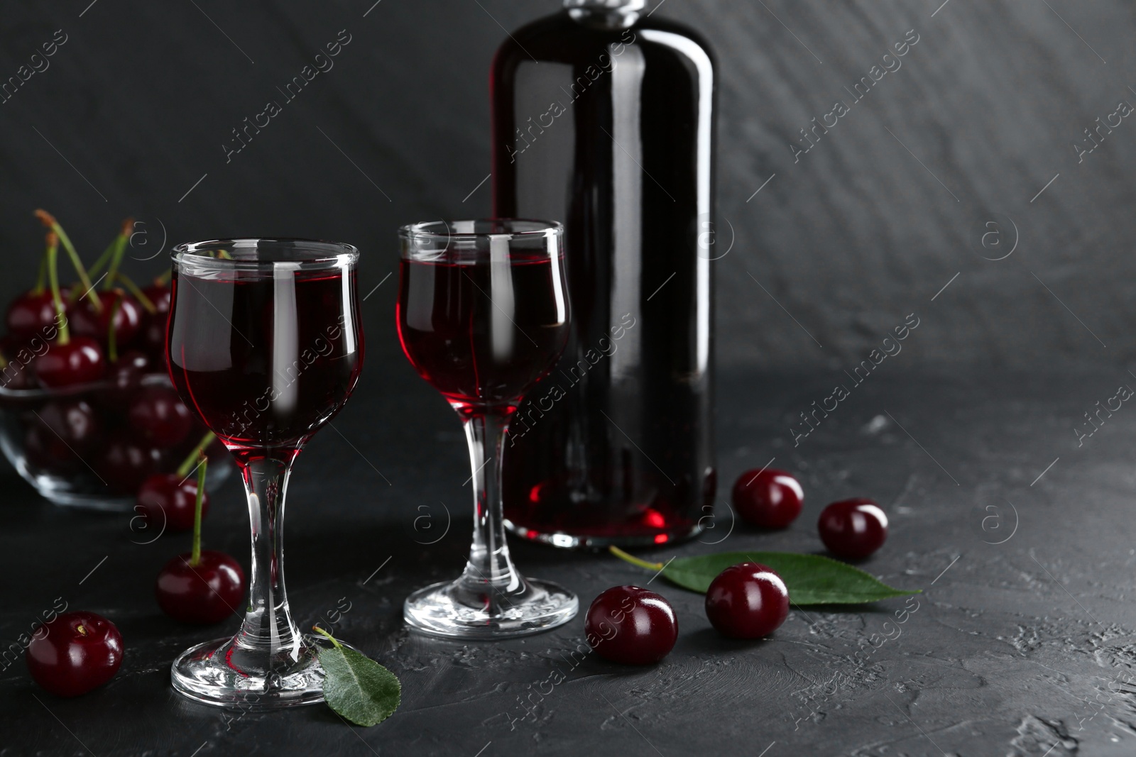 Photo of Delicious cherry liqueur and berries on black table