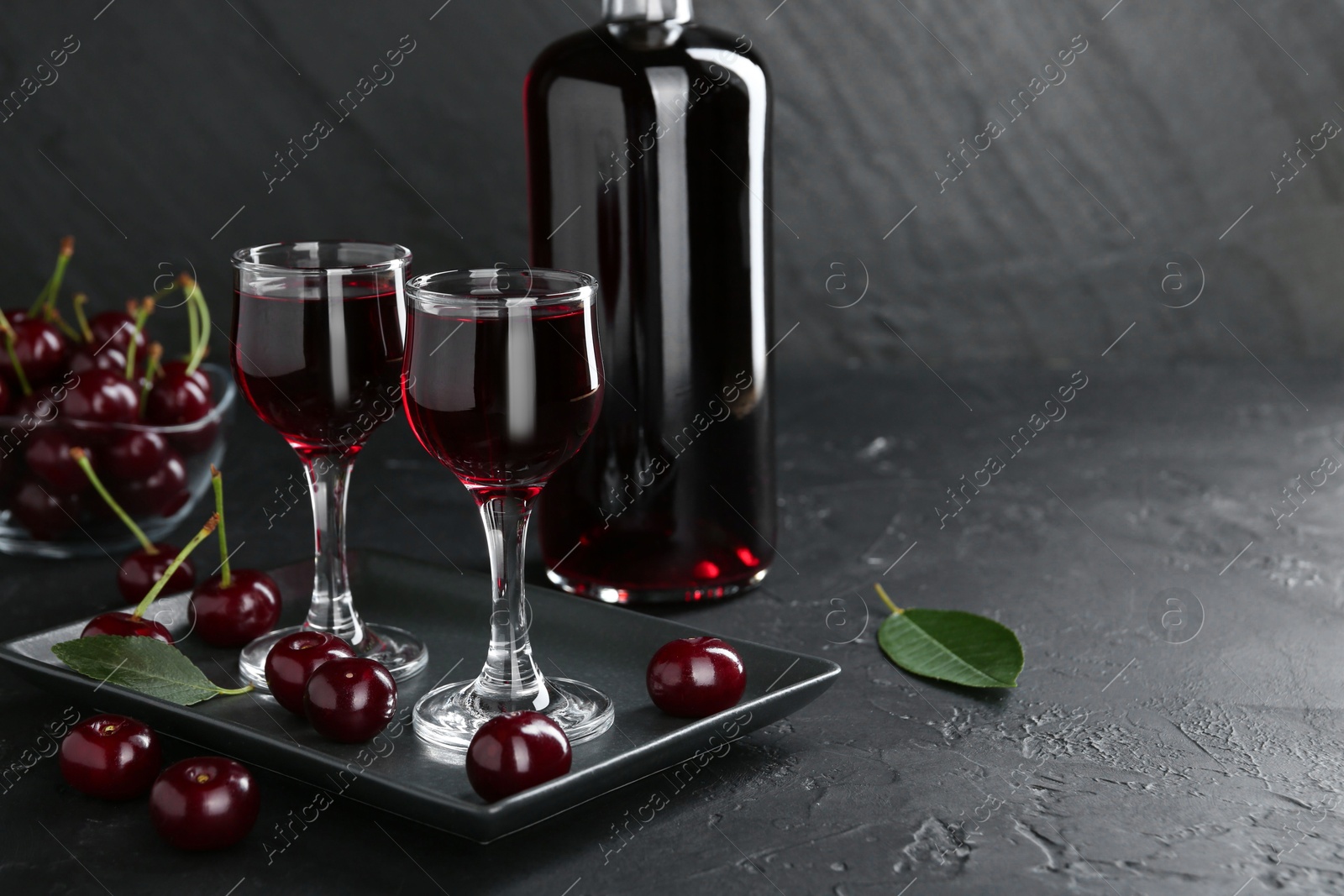 Photo of Delicious cherry liqueur and berries on black table