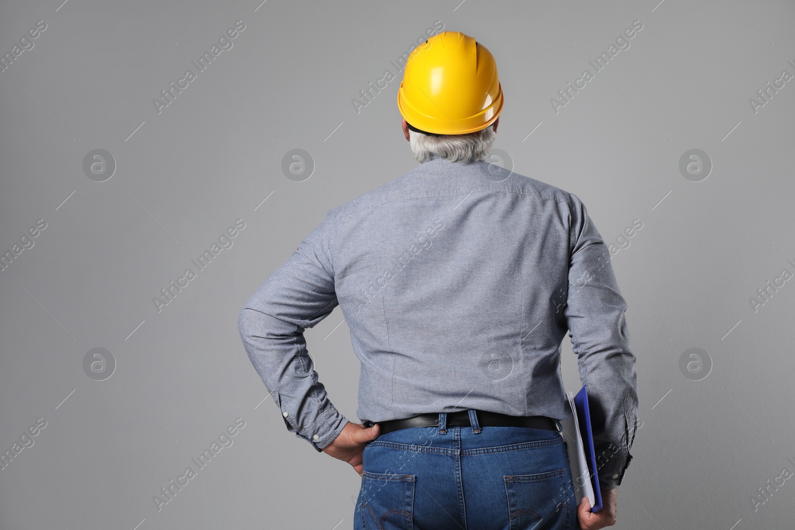 Photo of Engineer in hard hat with clipboard on grey background, back view