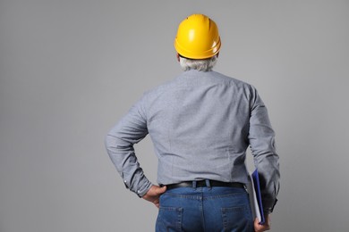 Engineer in hard hat with clipboard on grey background, back view