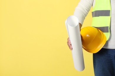 Engineer with hard hat and draft on yellow background, closeup. Space for text