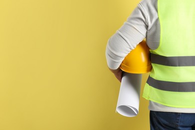 Engineer with hard hat and draft on yellow background, closeup. Space for text