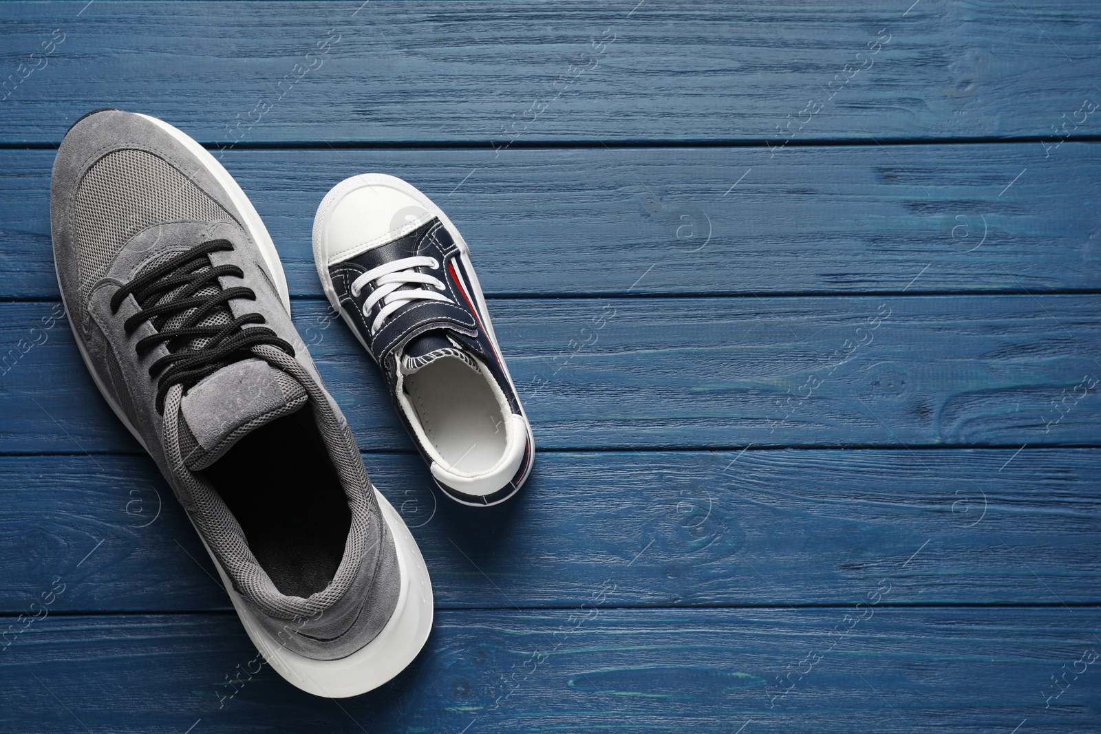 Photo of Big and small shoes on blue wooden table, top view. Space for text