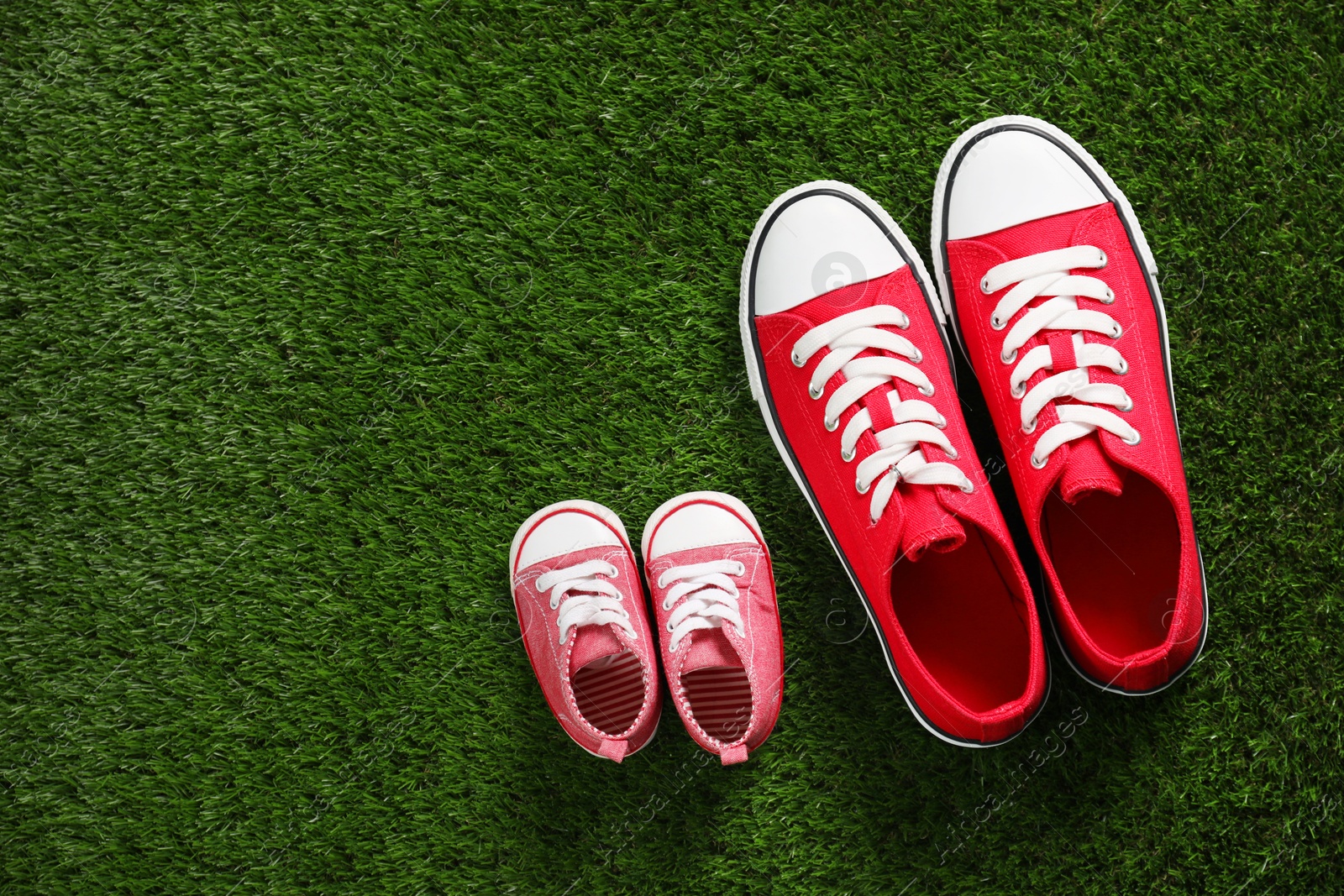 Photo of Big and small shoes on green grass, top view. Space for text