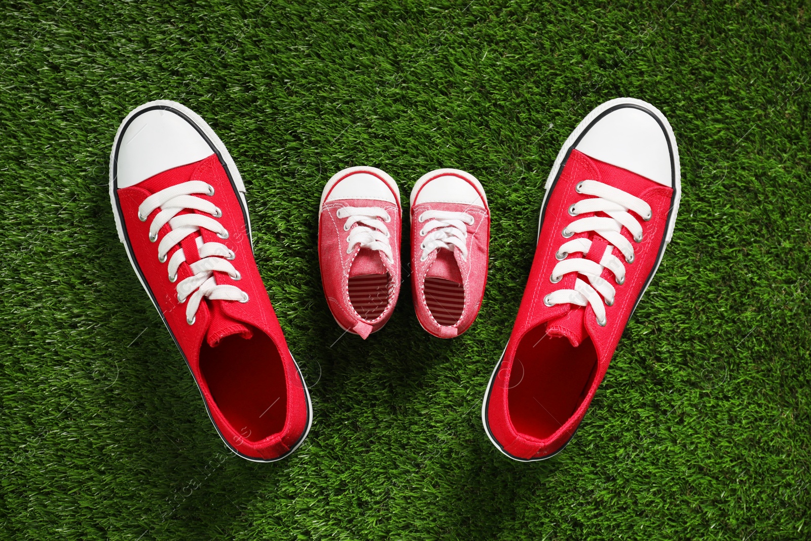 Photo of Big and small shoes on green grass, top view