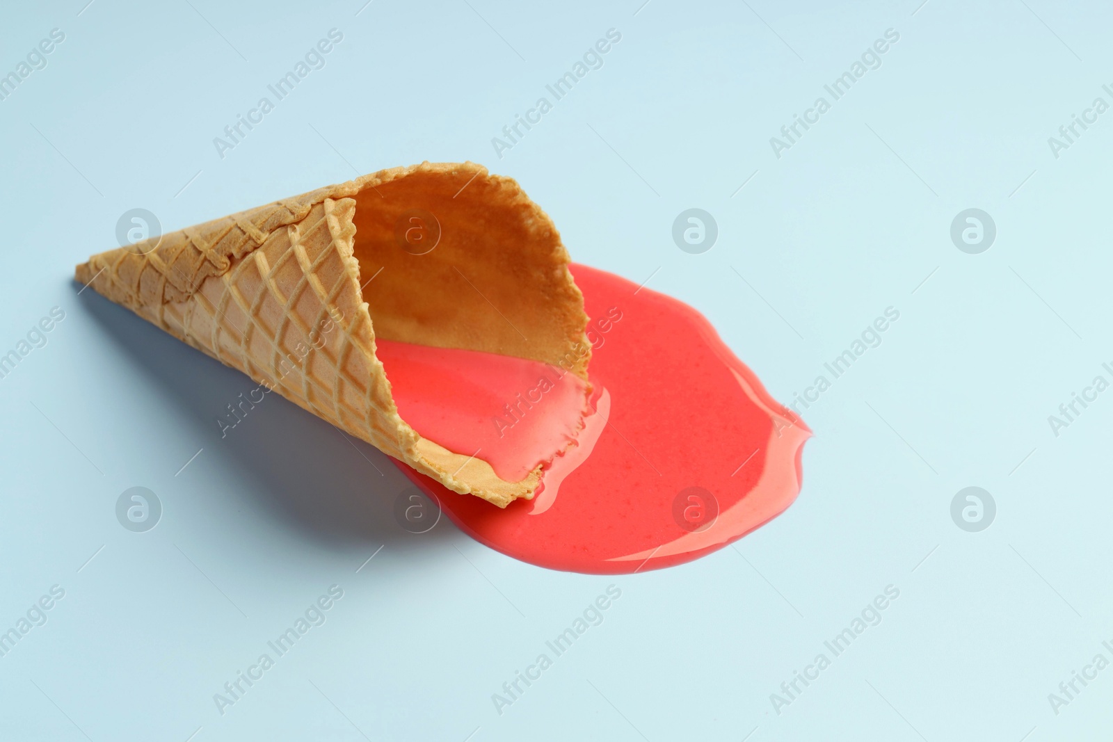 Photo of Melted ice cream and wafer cone on light blue background