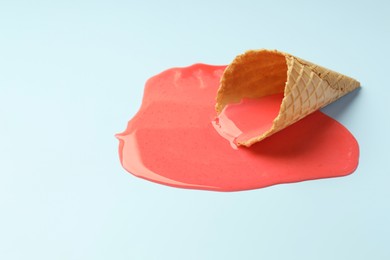 Melted ice cream and wafer cone on light blue background