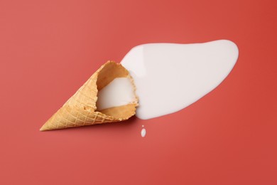 Melted ice cream and wafer cone on pale pink background, top view