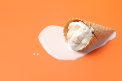 Photo of Melted ice cream in wafer cone on orange background. Space for text