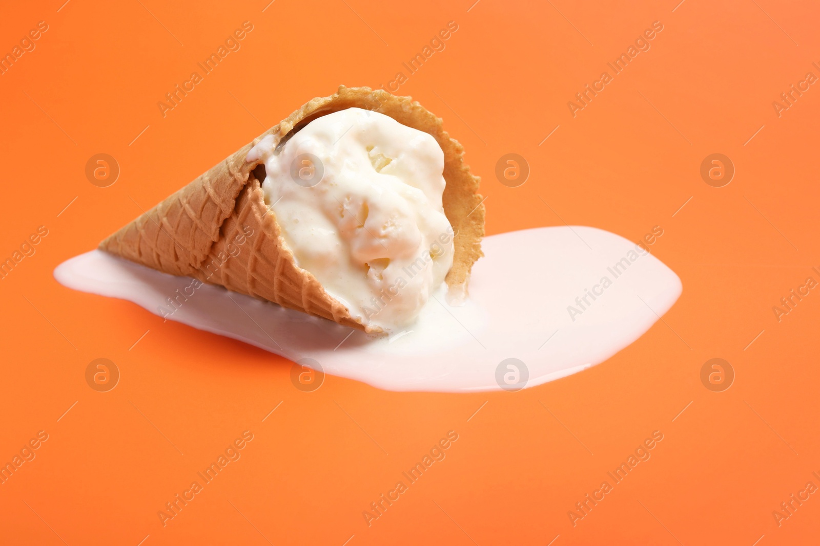 Photo of Melted ice cream in wafer cone on orange background. Space for text