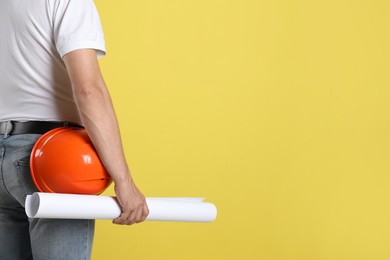 Engineer with hard hat and draft on yellow background, closeup. Space for text