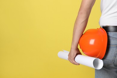 Engineer with hard hat and draft on yellow background, closeup. Space for text