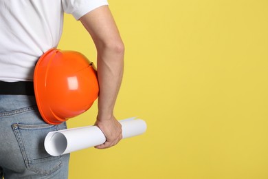 Engineer with hard hat and draft on yellow background, closeup. Space for text