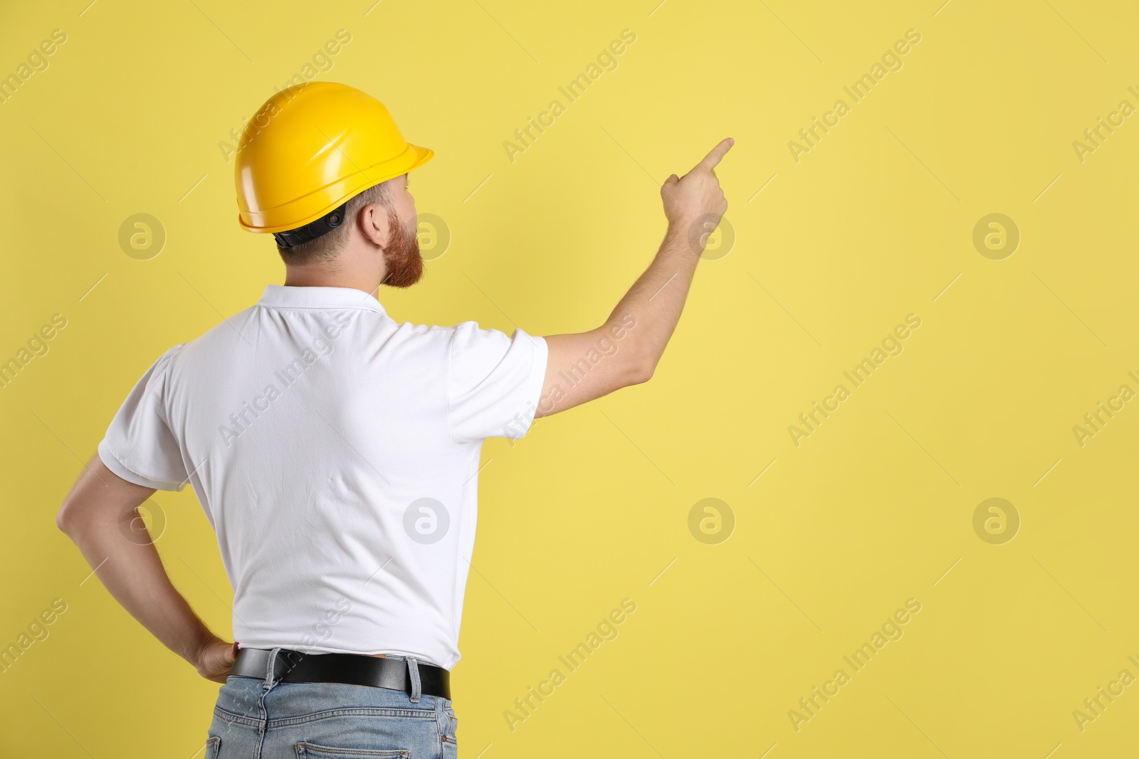 Photo of Engineer in hard hat pointing at something on yellow background, space for text