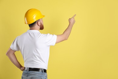 Engineer in hard hat pointing at something on yellow background, space for text