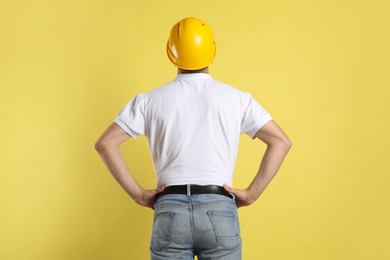 Engineer in hard hat on yellow background, back view