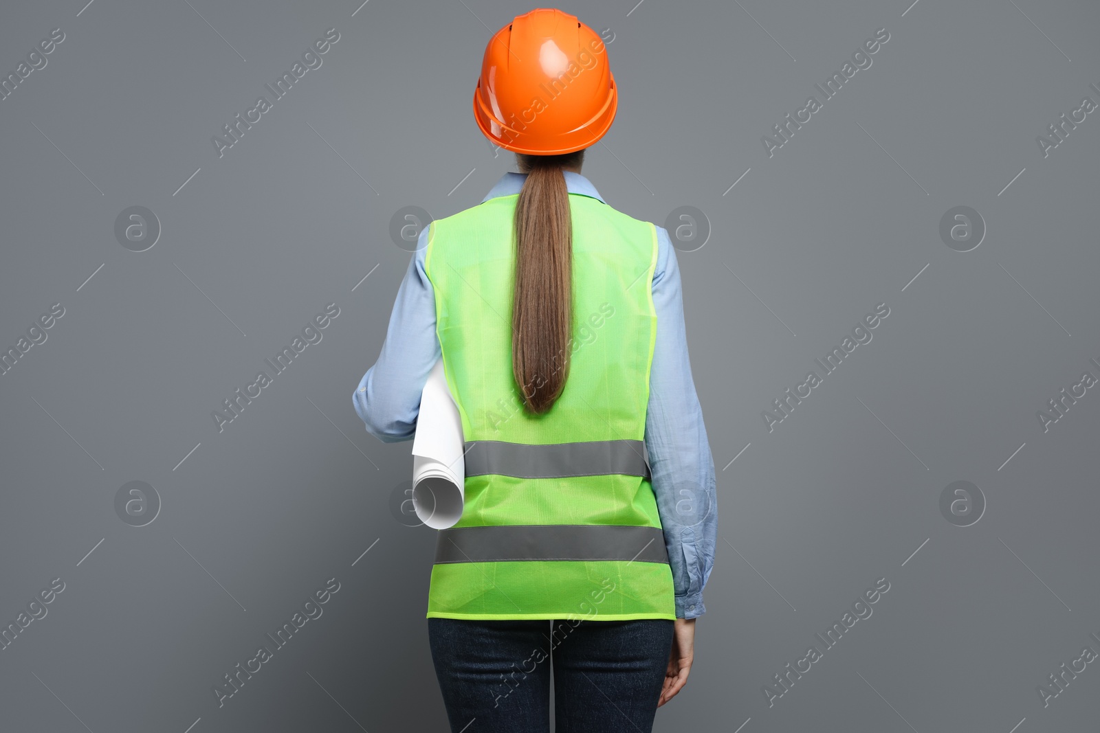 Photo of Engineer in hard hat with draft on grey background, back view