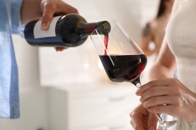 Man pouring red wine into woman`s glass indoors, selective focus