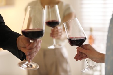 Friends with glasses of red wine indoors, selective focus