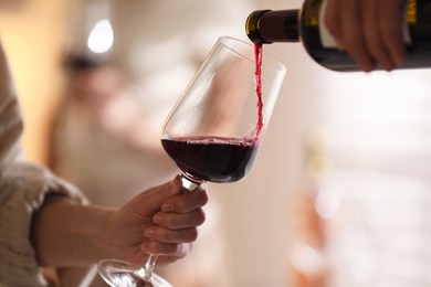 Photo of Man pouring red wine into woman`s glass indoors, selective focus