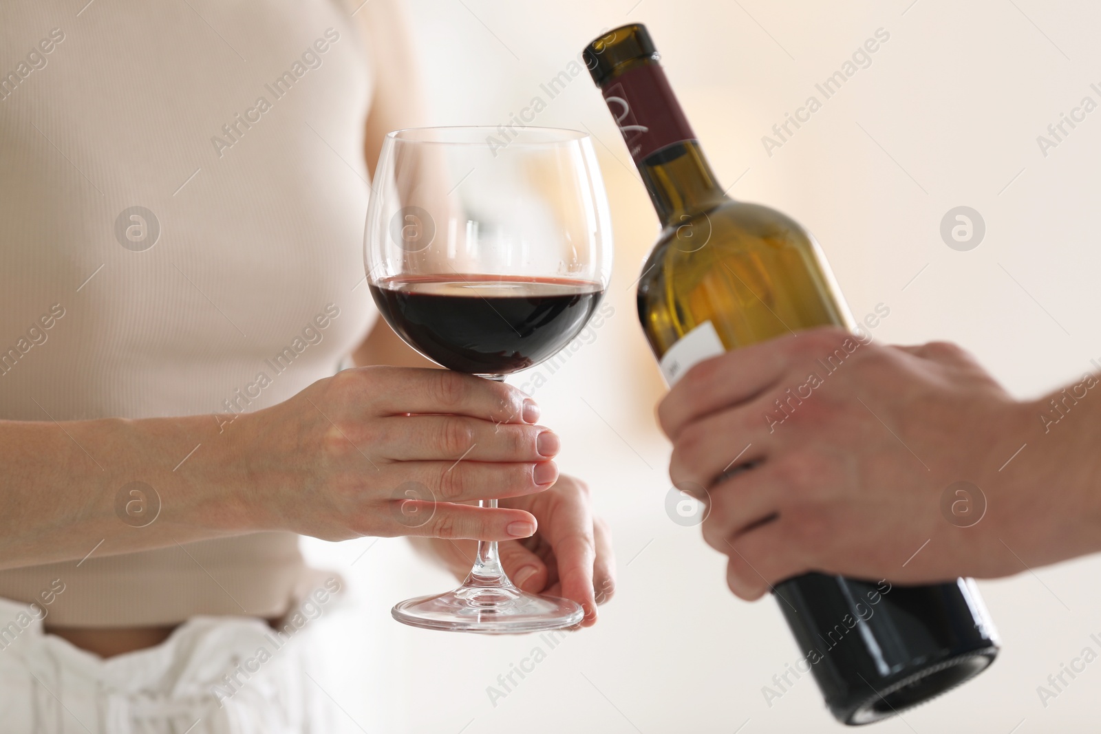 Photo of Man pouring red wine into woman`s glass indoors, closeup