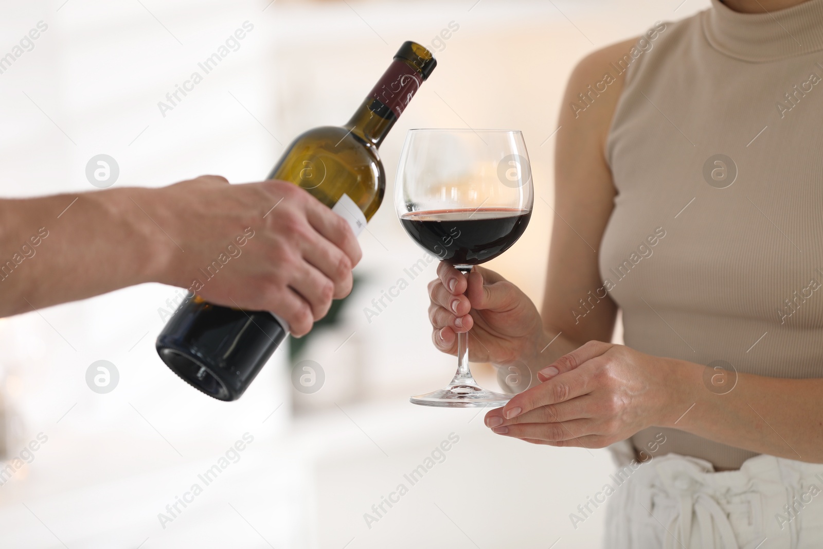 Photo of Man pouring red wine into woman`s glass indoors, closeup