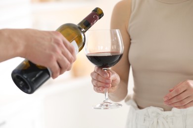 Photo of Man pouring red wine into woman`s glass indoors, closeup