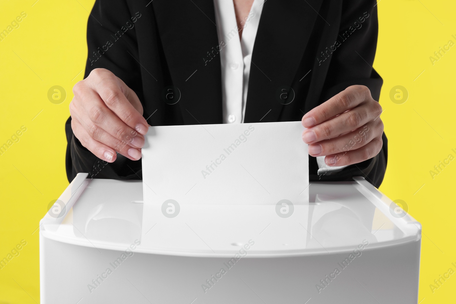 Photo of Woman putting her vote into ballot box against yellow background, closeup