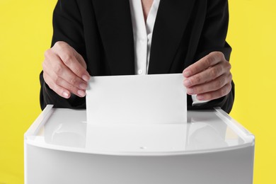 Photo of Woman putting her vote into ballot box against yellow background, closeup