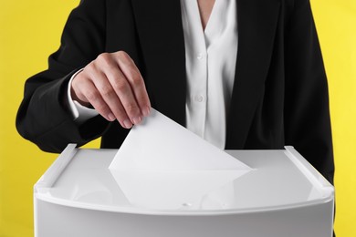 Photo of Woman putting her vote into ballot box against yellow background, closeup