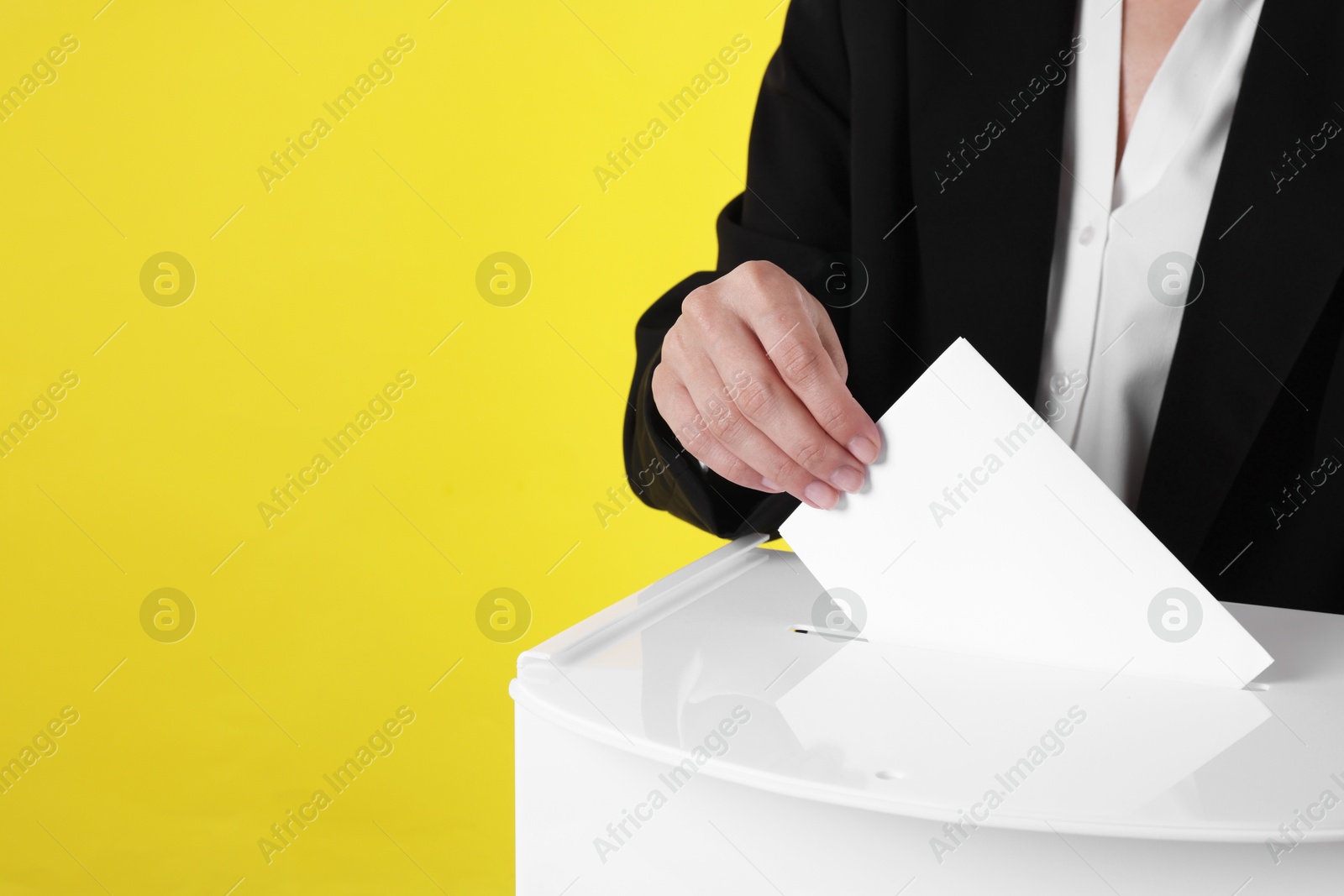 Photo of Woman putting her vote into ballot box against yellow background, closeup. Space for text