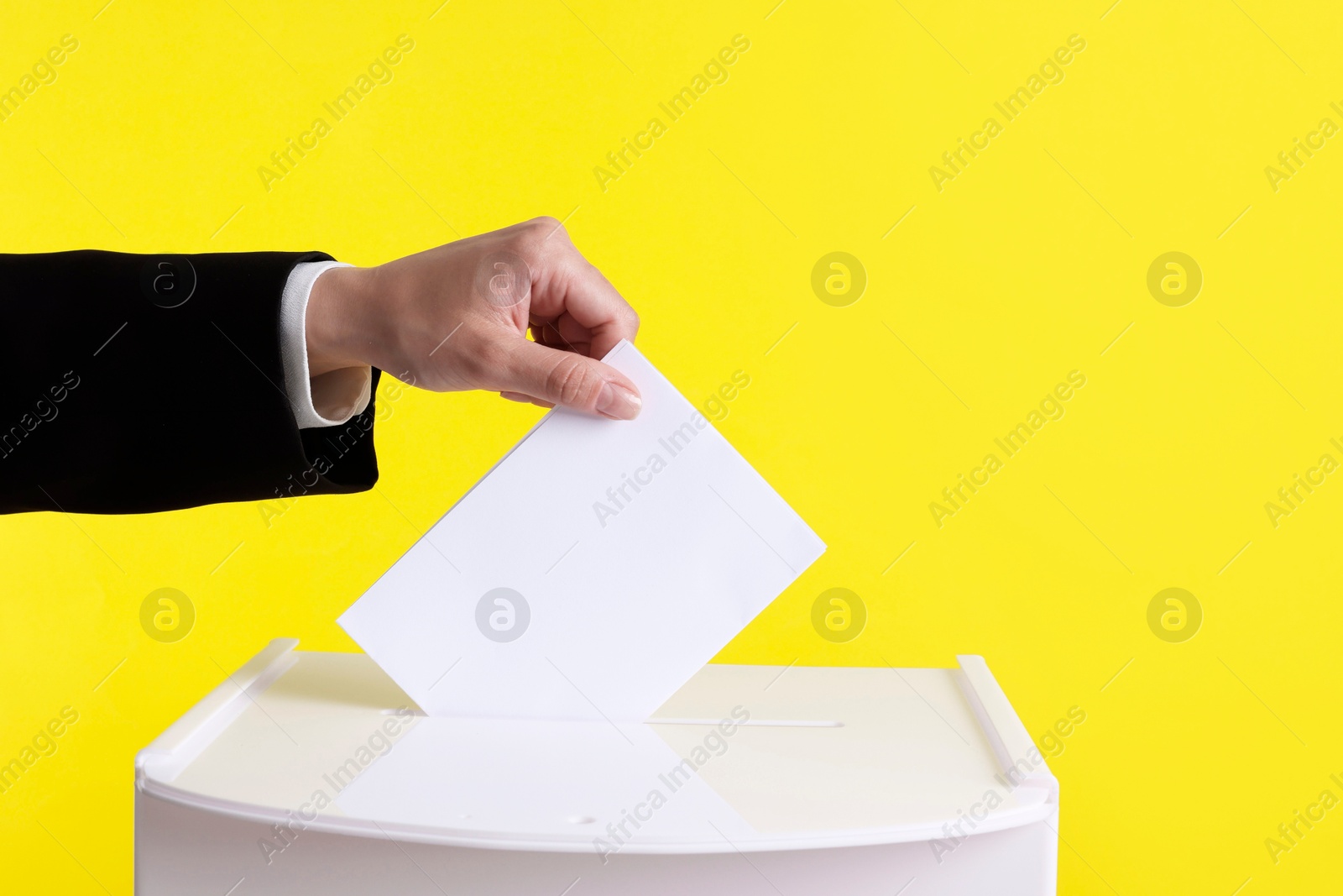 Photo of Woman putting her vote into ballot box against yellow background, closeup. Space for text