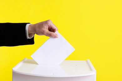 Photo of Woman putting her vote into ballot box against yellow background, closeup. Space for text