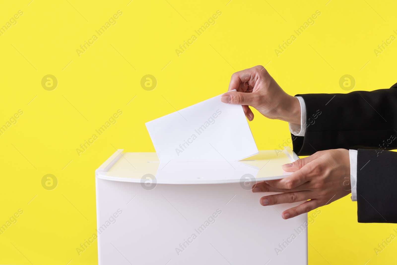 Photo of Woman putting her vote into ballot box against yellow background, closeup