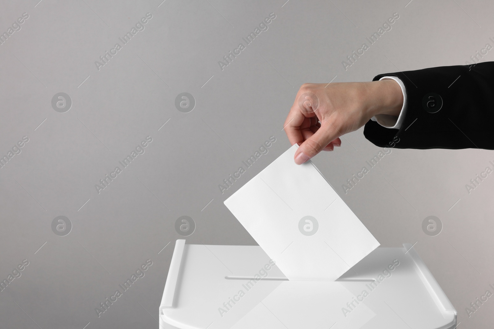 Photo of Woman putting her vote into ballot box against grey background, closeup. Space for text