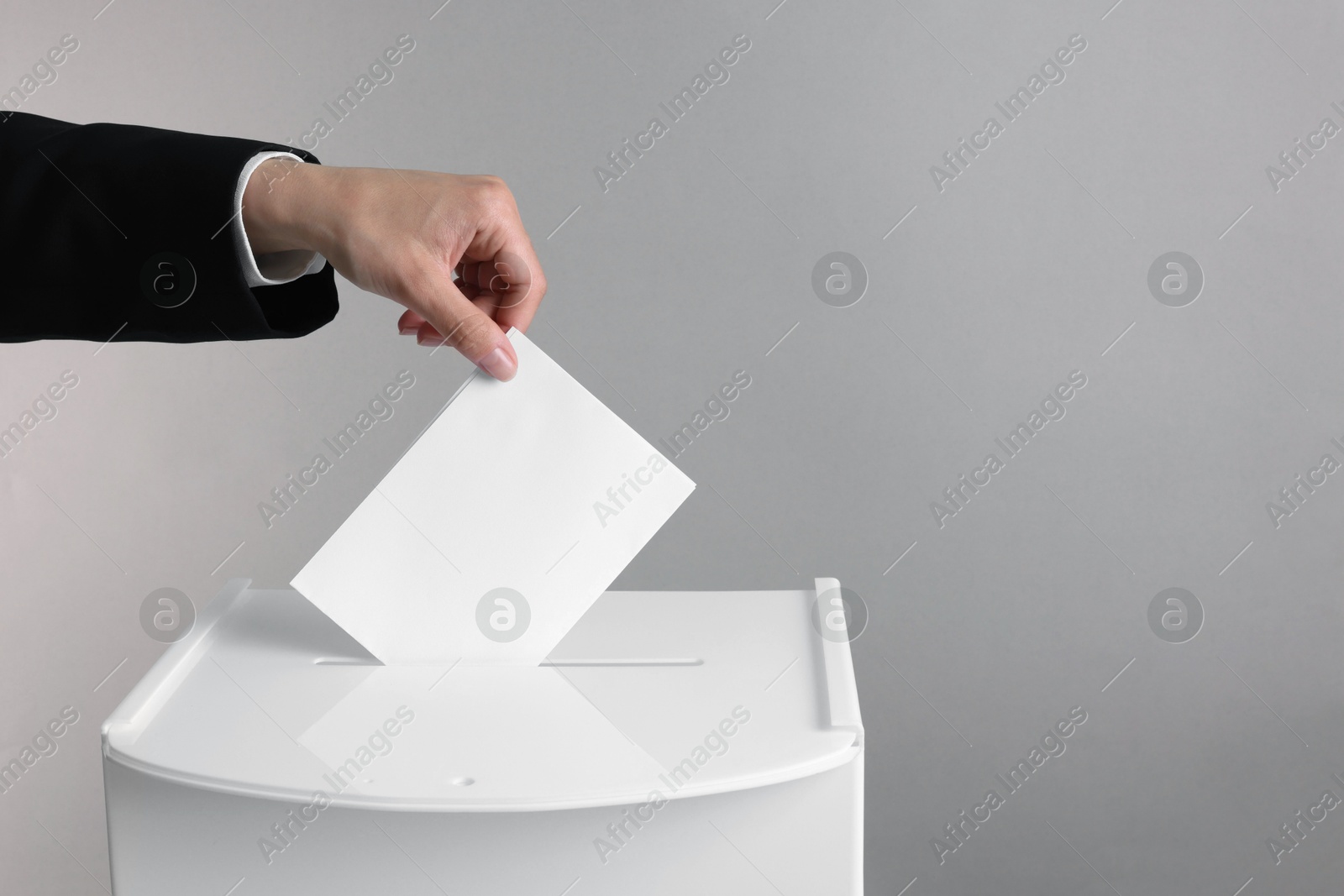 Photo of Woman putting her vote into ballot box against grey background, closeup. Space for text