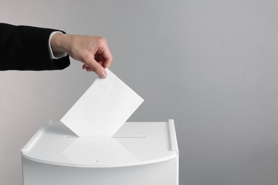 Photo of Woman putting her vote into ballot box against grey background, closeup. Space for text