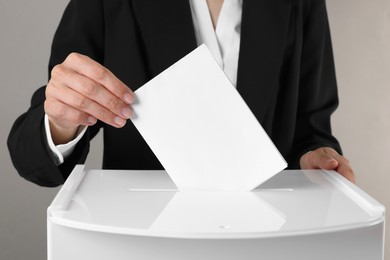 Photo of Woman putting her vote into ballot box against grey background, closeup