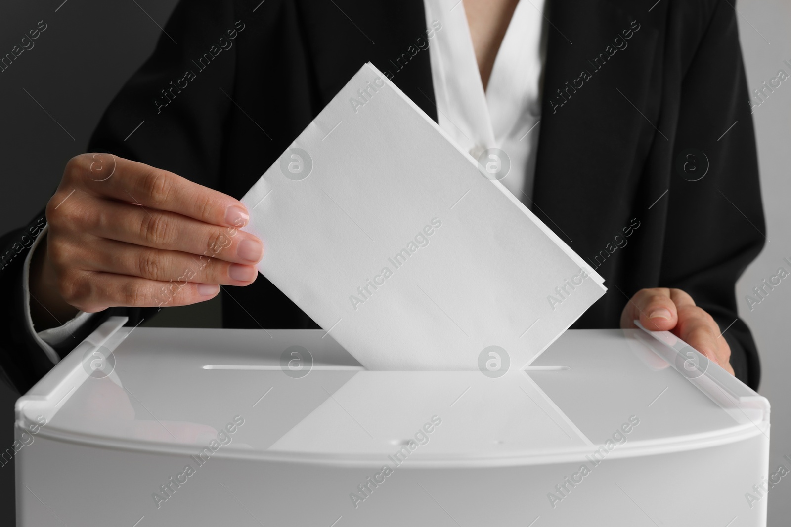 Photo of Woman putting her vote into ballot box against grey background, closeup