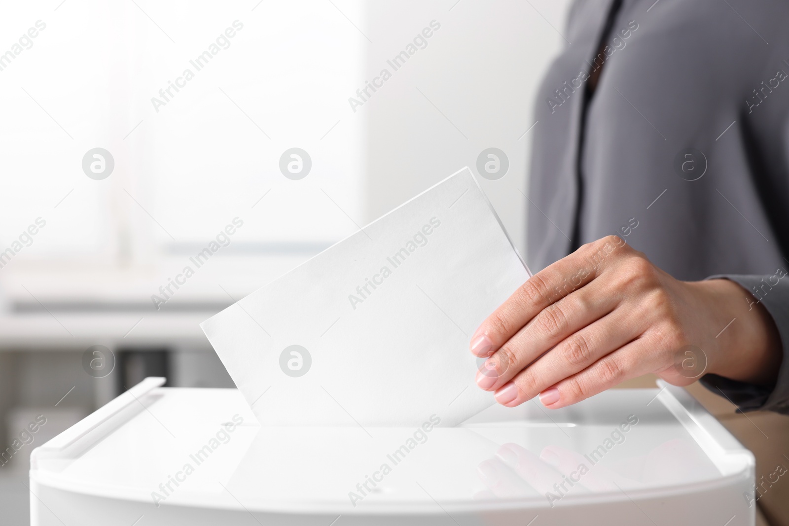 Photo of Woman putting her vote into ballot box indoors, closeup