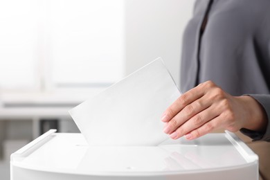 Photo of Woman putting her vote into ballot box indoors, closeup