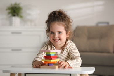 Portrait of smiling girl playing with wooden geometric figures at table indoors. Adorable child