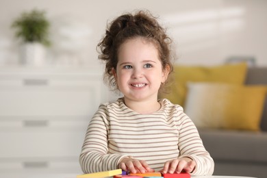 Portrait of smiling girl playing with wooden geometric figures at table indoors. Adorable child