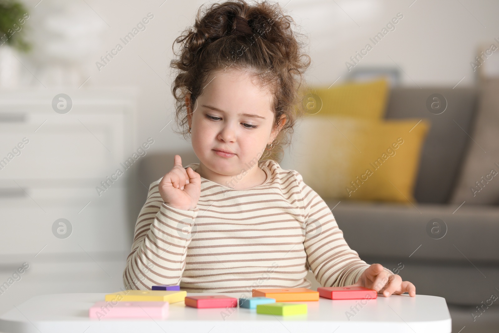 Photo of Portrait of cute girl playing with wooden geometric figures at table indoors. Adorable child