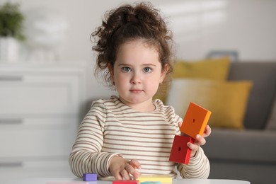 Portrait of cute girl playing with wooden geometric figures at table indoors. Adorable child