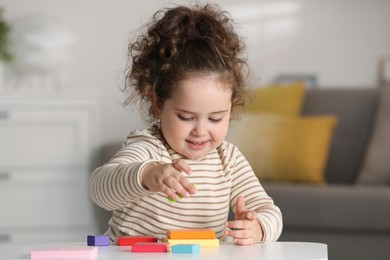 Photo of Portrait of cute girl playing with wooden geometric figures at table indoors. Adorable child