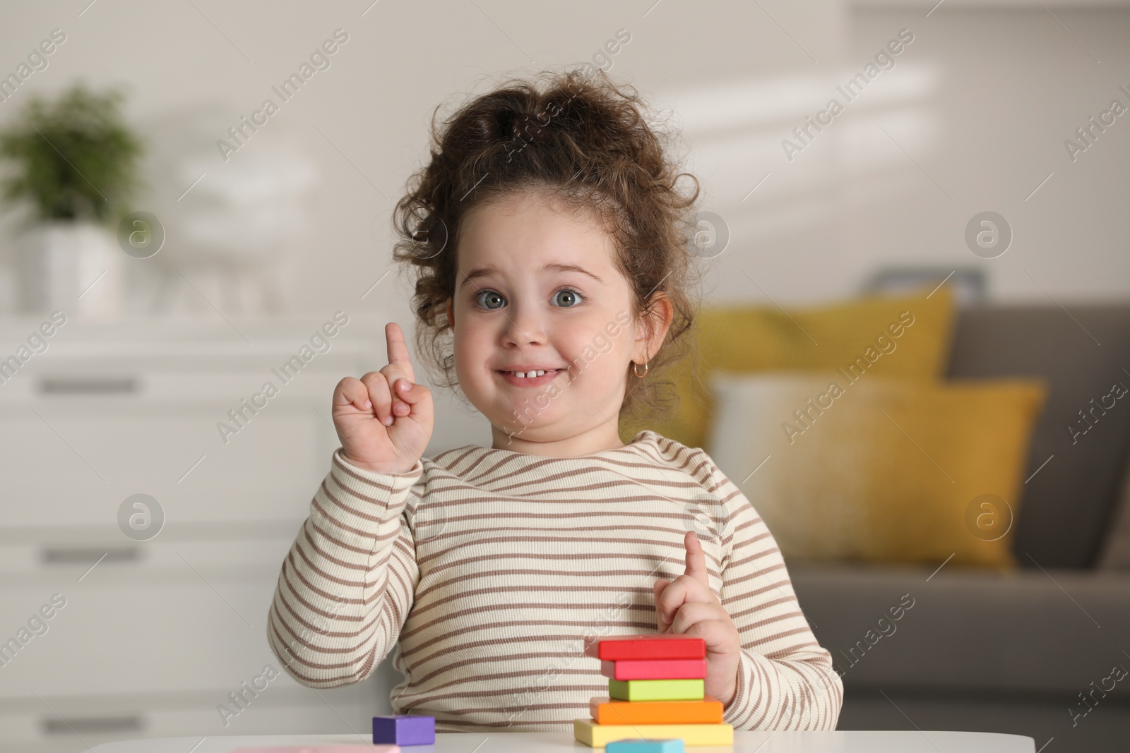 Photo of Portrait of smiling girl playing with wooden geometric figures at table indoors. Adorable child