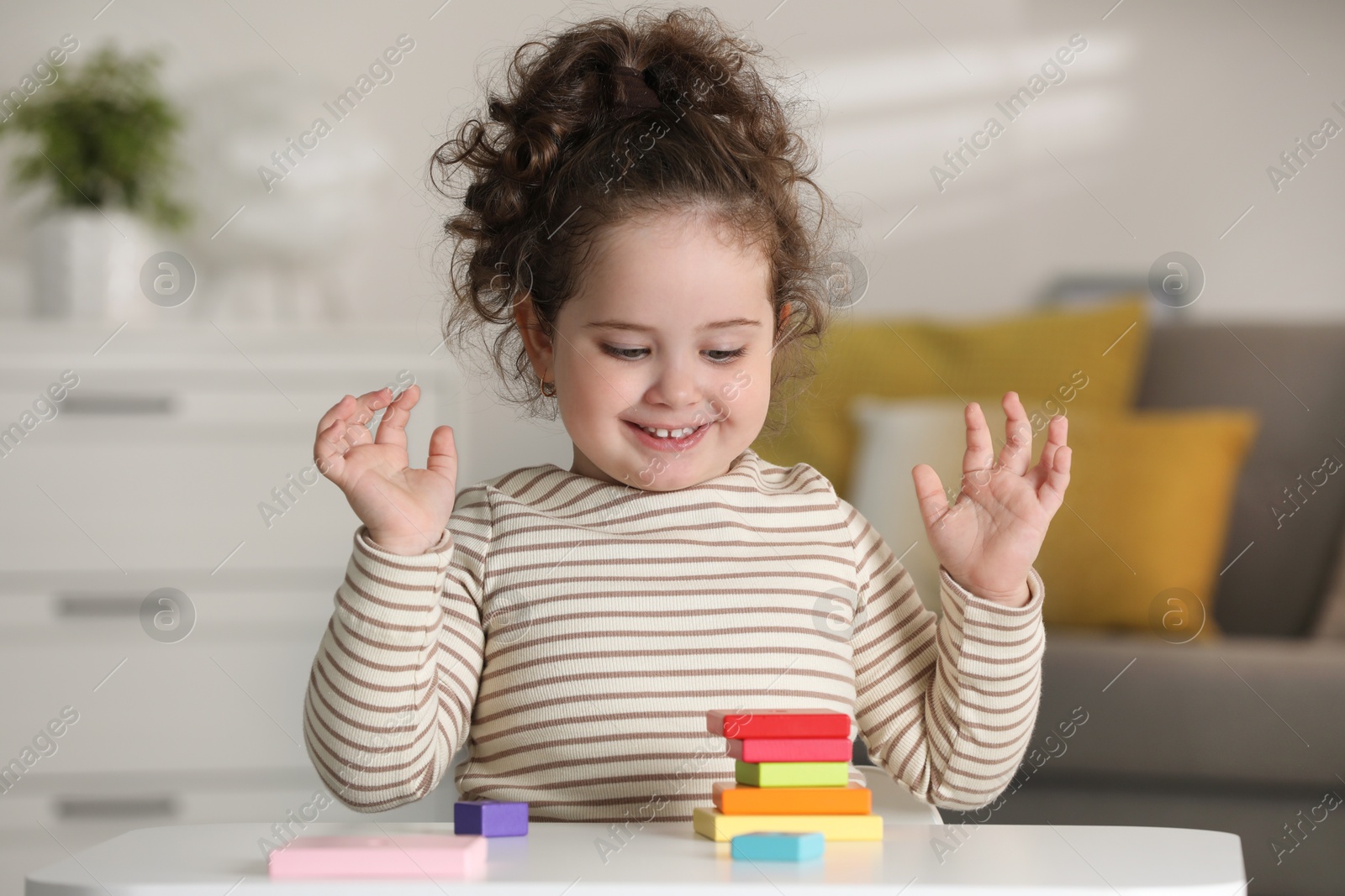 Photo of Portrait of smiling girl playing with wooden geometric figures at table indoors. Adorable child