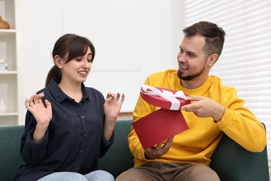 Photo of Smiling man presenting gift to embarrassed woman at home