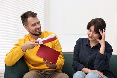 Photo of Smiling man presenting gift to embarrassed woman at home